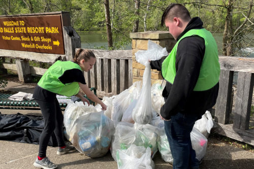 Two volunteers piling up trash bags filled with litter